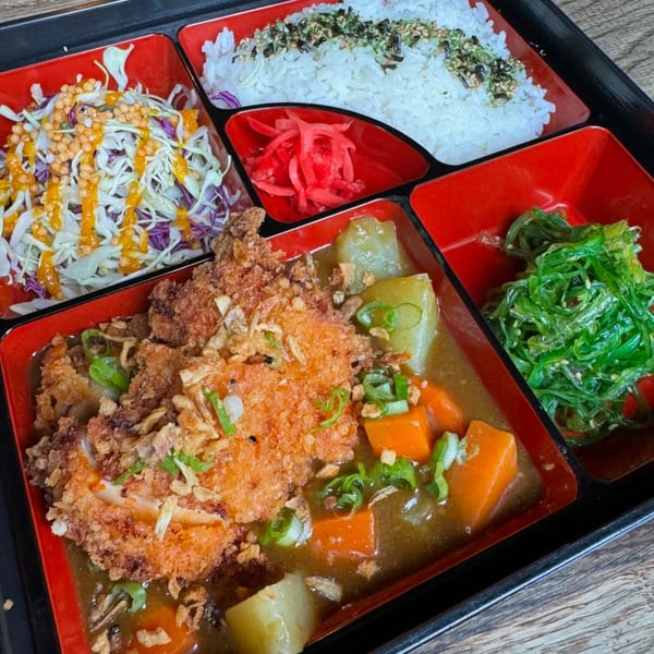 Japanese bento box with chicken katsu curry, rice, cabbage salad, seaweed salad, and pickled ginger.