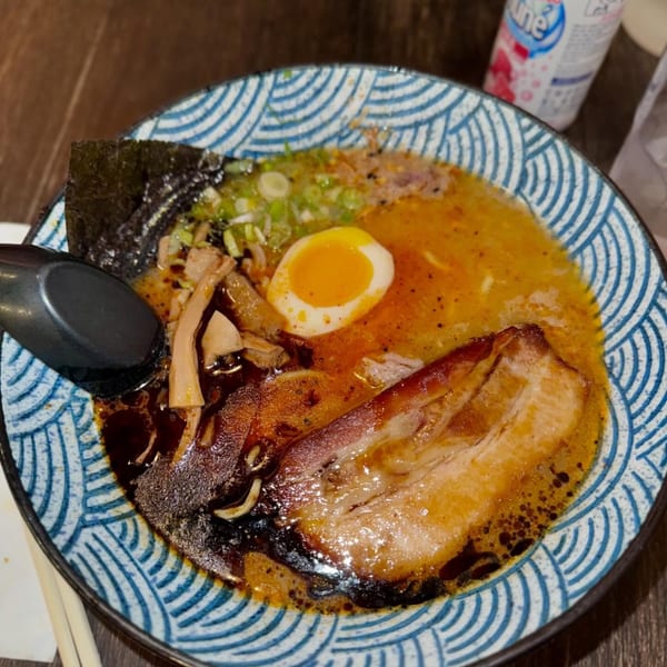A bowl of ramen with pork belly, a soft-boiled egg, seaweed, and green onions.